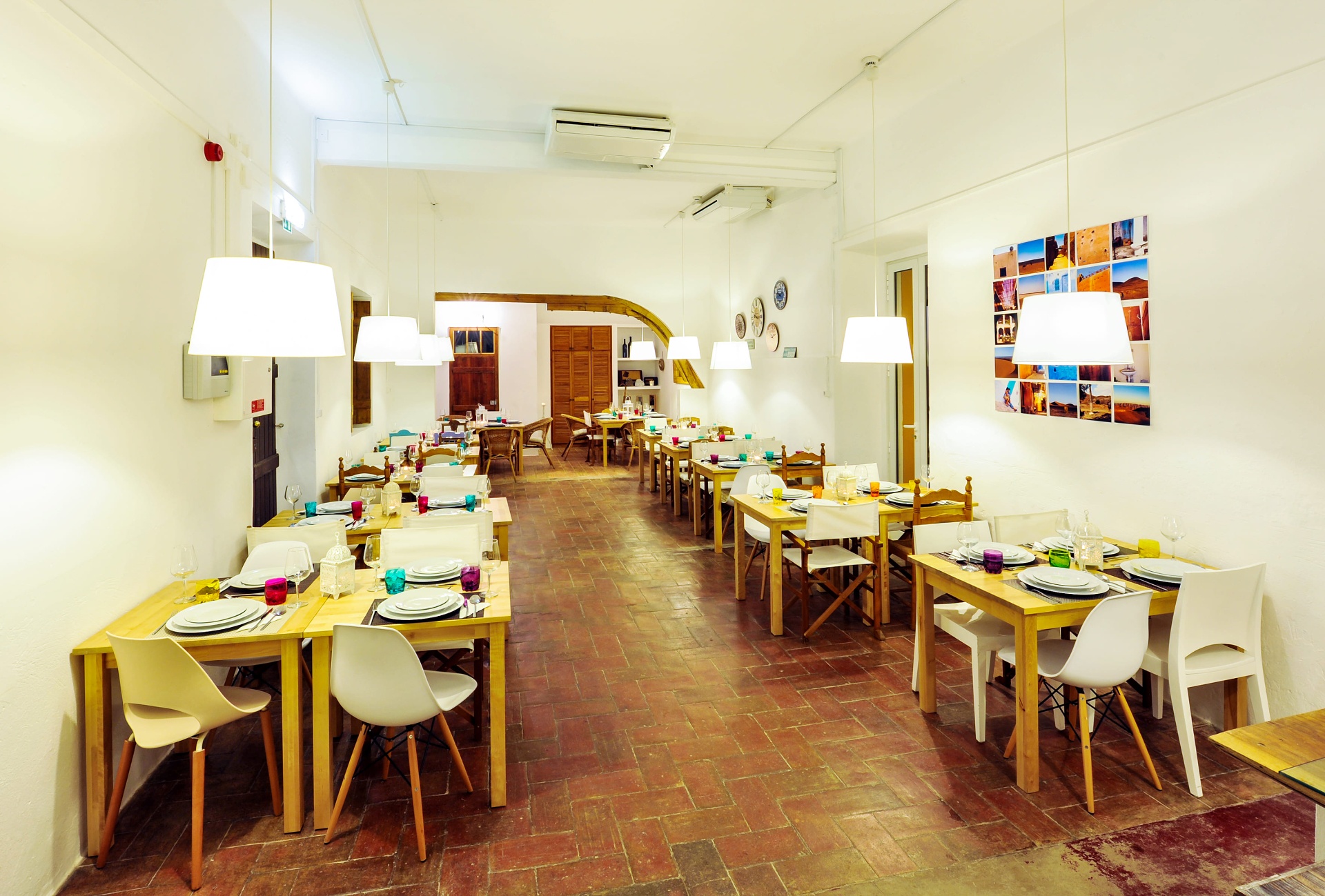 Sala de jantar do restaurante com mesas de madeira, candeeiros suspensos e chão em tijoleira