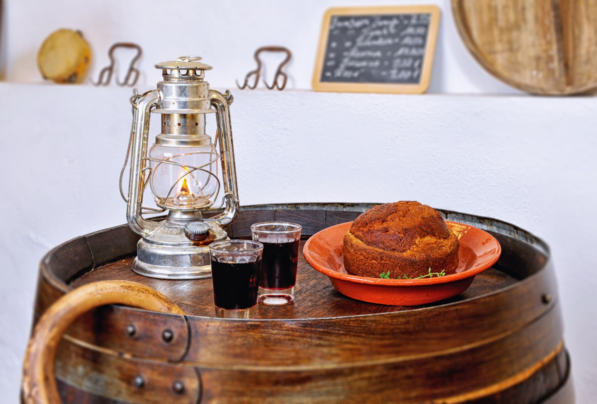 Bolo do caco caseiro com dois copos de vinho tinto e candeeiro a petróleo sobre uma pipa de madeira